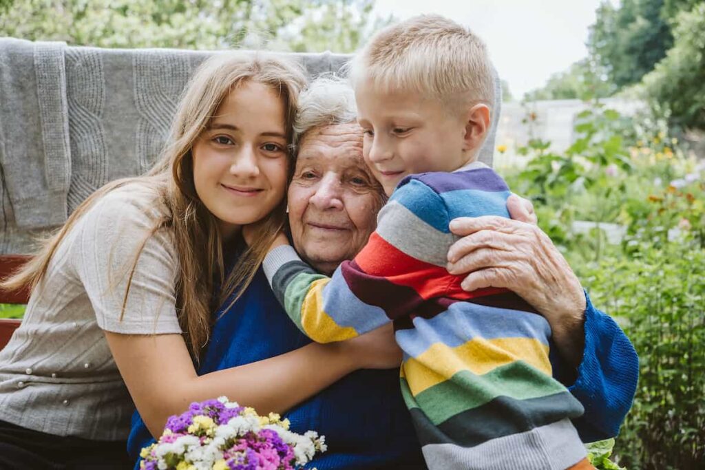 Abuela abrazada por sus nietos al aire libre